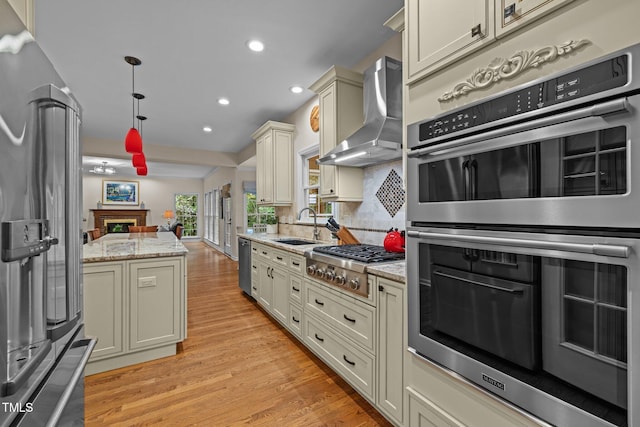 kitchen featuring appliances with stainless steel finishes, ventilation hood, light wood finished floors, recessed lighting, and a sink