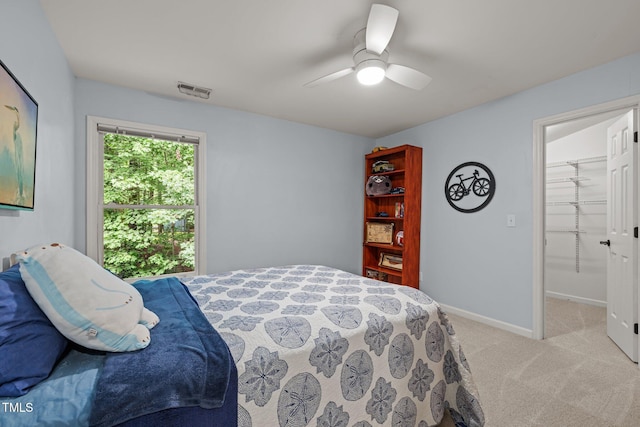 bedroom featuring light colored carpet, a ceiling fan, baseboards, and a walk in closet