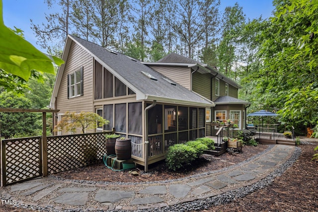 rear view of property featuring a sunroom, a wooden deck, and a shingled roof