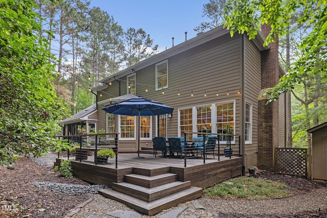 back of property with a deck, a chimney, and outdoor dining space