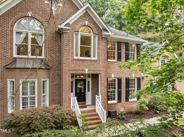 georgian-style home featuring cooling unit and brick siding
