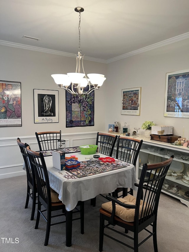 carpeted dining area with a wainscoted wall, visible vents, crown molding, and a notable chandelier