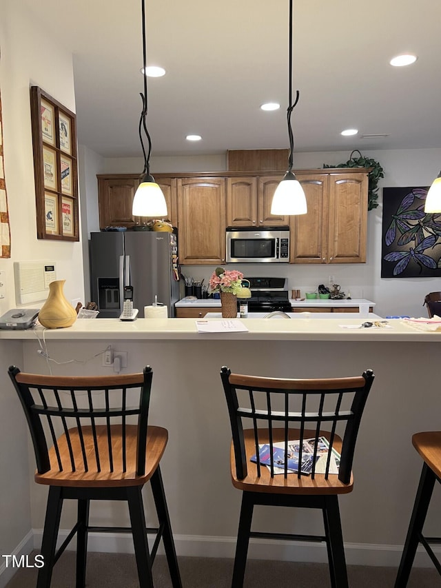 kitchen with appliances with stainless steel finishes, a breakfast bar, light countertops, and hanging light fixtures