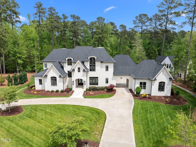 french provincial home featuring stucco siding, curved driveway, a front yard, and roof with shingles