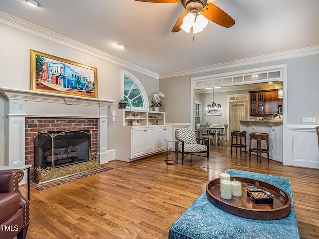 5401 Fire Pink Way, Raleigh, NC 27613 - living room featuring ornamental molding, wood finished floors, ceiling fan, a brick fireplace, and a wainscoted wall