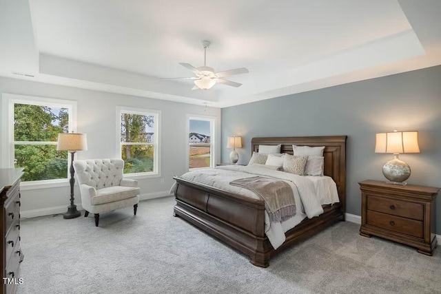 bedroom with light colored carpet, baseboards, multiple windows, and a raised ceiling