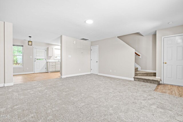 1628 Briarmont Ct, Raleigh, NC 27610 - unfurnished living room with light wood-style flooring, visible vents, baseboards, light carpet, and stairs