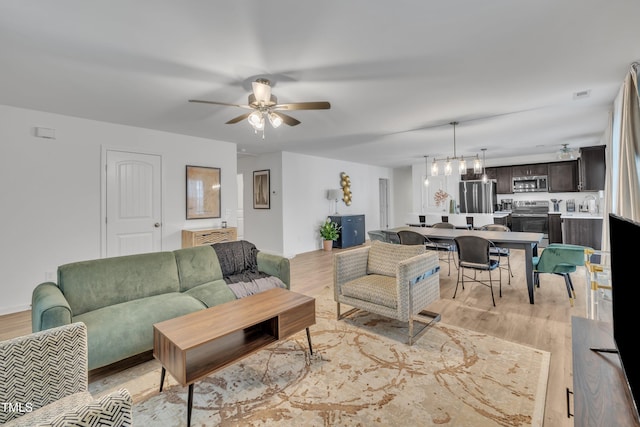 living area with light wood-style floors, ceiling fan with notable chandelier, and visible vents