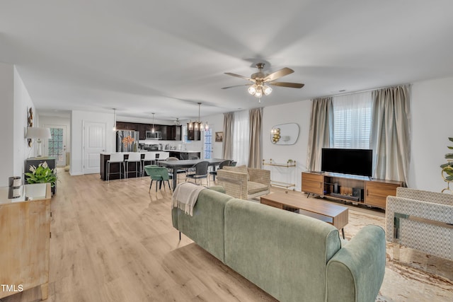 living room featuring ceiling fan with notable chandelier and light wood-style flooring