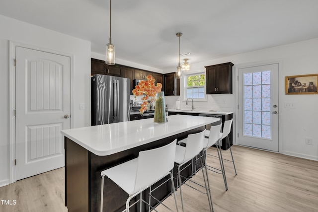 kitchen with dark brown cabinets, a sink, light wood-style floors, light countertops, and stainless steel appliances