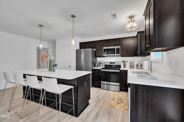 kitchen featuring a kitchen breakfast bar, a sink, light countertops, light wood finished floors, and stainless steel appliances