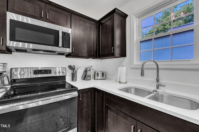 kitchen featuring light countertops, dark brown cabinetry, appliances with stainless steel finishes, and a sink