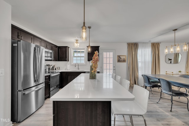 kitchen with dark brown cabinetry, a kitchen island, a sink, stainless steel appliances, and light wood-style flooring