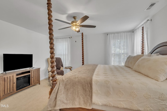 bedroom with visible vents, a glass covered fireplace, ceiling fan, and light colored carpet