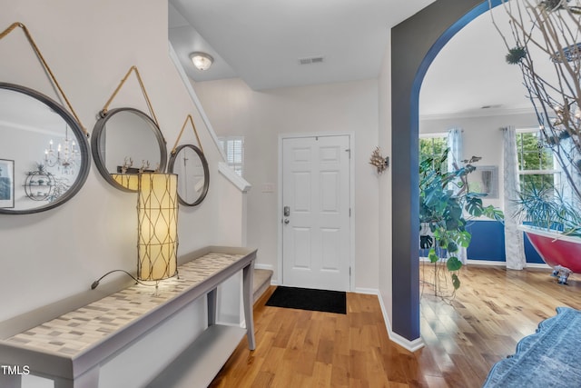 entryway with wood finished floors, baseboards, arched walkways, and ornamental molding