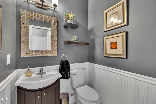 bathroom with wainscoting, vanity, toilet, and a decorative wall