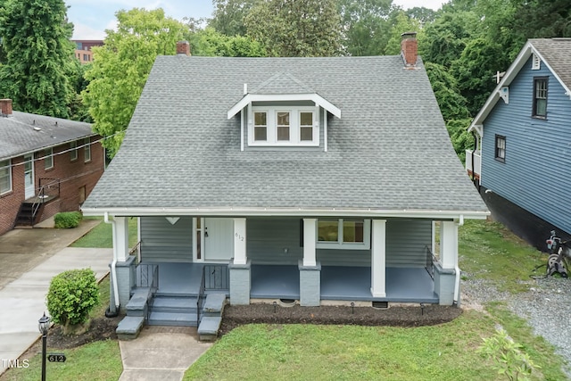view of front of home with a porch, a chimney, a shingled roof, and a front yard
