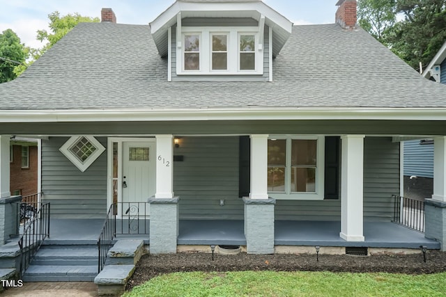 bungalow-style house featuring covered porch, a shingled roof, and a chimney