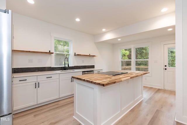 kitchen with open shelves, wooden counters, a sink, a center island, and white cabinets