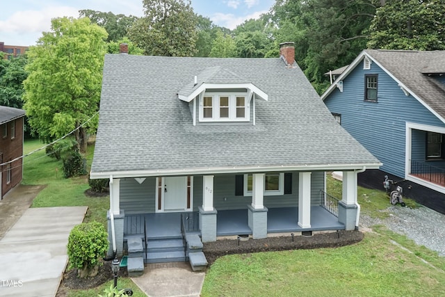 view of front facade featuring covered porch, a chimney, a shingled roof, and a front lawn