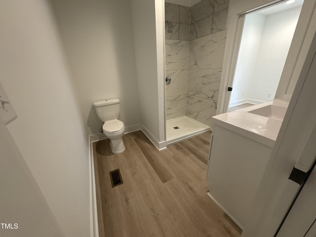 bathroom featuring wood finished floors, toilet, a marble finish shower, vanity, and baseboards