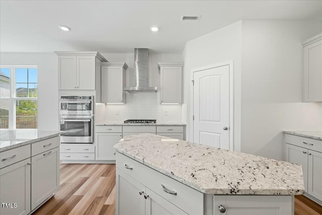 1005 Whispering Creek Ct, Knightdale, NC 27545 - kitchen with stainless steel appliances, light wood-style flooring, visible vents, wall chimney range hood, and a kitchen island