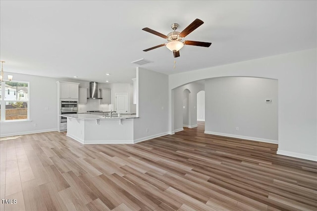 1005 Whispering Creek Ct, Knightdale, NC 27545 - unfurnished living room featuring ceiling fan with notable chandelier, arched walkways, a sink, and light wood-style flooring
