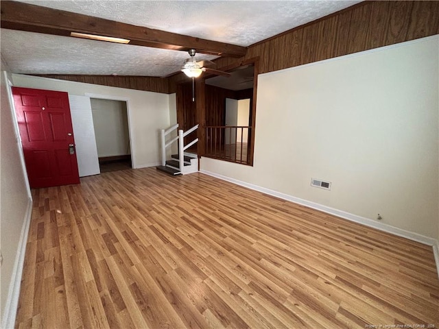 unfurnished living room featuring baseboards, beam ceiling, light wood-style floors, and visible vents