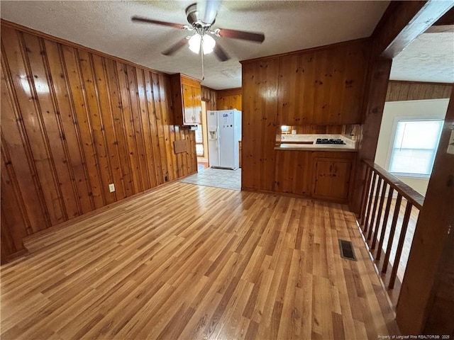 interior space featuring wood walls, a ceiling fan, a textured ceiling, and light wood-style flooring