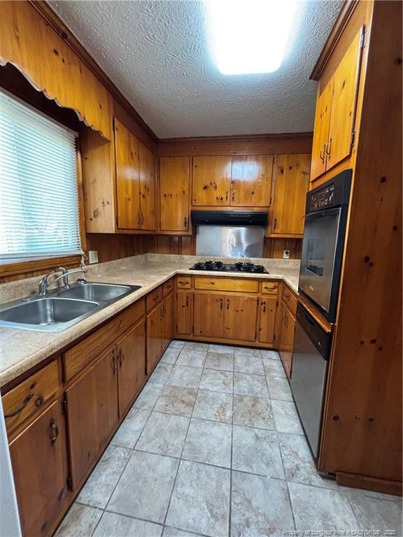 kitchen with brown cabinets, under cabinet range hood, a sink, black appliances, and a textured ceiling
