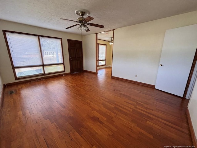 spare room with a textured ceiling, wood finished floors, visible vents, and baseboards