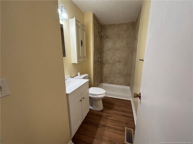 bathroom with toilet, wood finished floors, visible vents, and a tile shower