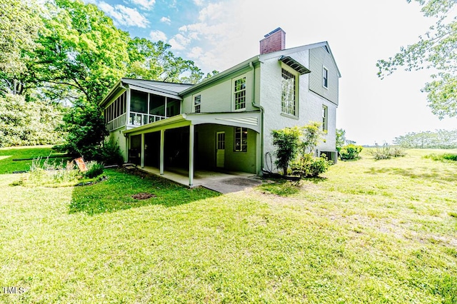 rear view of property with a yard, central AC unit, a chimney, and a sunroom