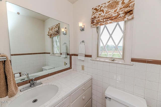 half bathroom featuring vanity, a wainscoted wall, toilet, and tile walls