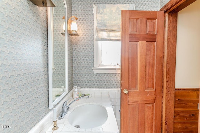 bathroom featuring a sink, wainscoting, and wallpapered walls