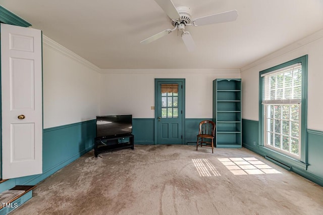 sitting room featuring carpet flooring, crown molding, ceiling fan, and a wainscoted wall