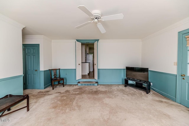 unfurnished living room featuring carpet floors, a ceiling fan, wainscoting, and crown molding