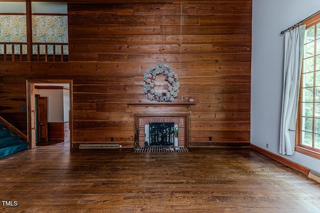 unfurnished living room featuring wood walls, a brick fireplace, wood finished floors, and stairway