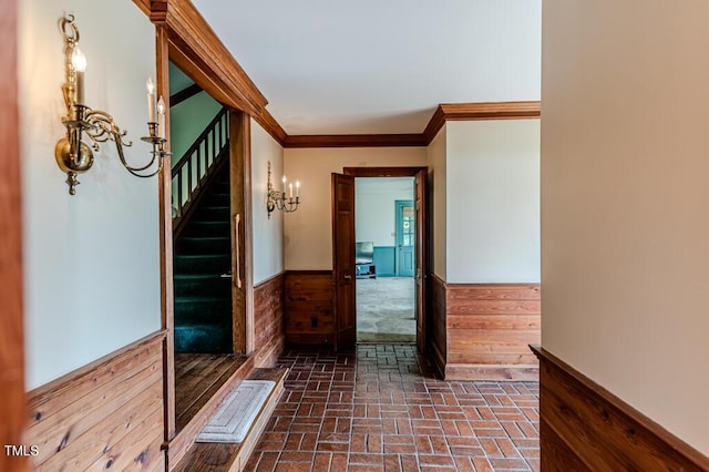 hallway with crown molding, brick floor, wainscoting, and stairs