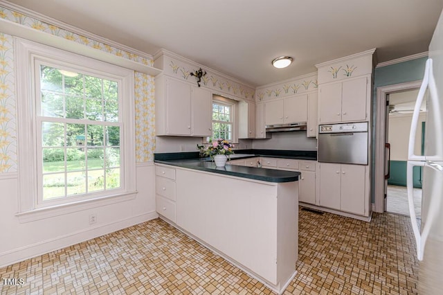kitchen with dark countertops, wall oven, a peninsula, under cabinet range hood, and white cabinetry