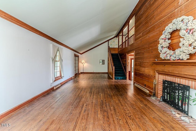 unfurnished living room with crown molding, wooden walls, wood finished floors, vaulted ceiling, and stairway
