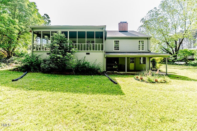 rear view of house with a yard, a chimney, a sunroom, and a carport
