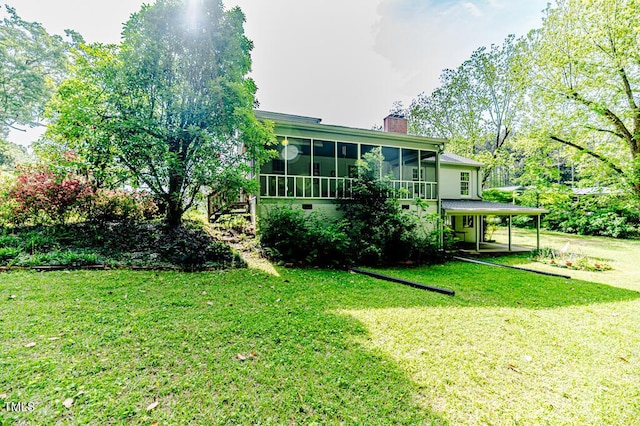 exterior space featuring an attached carport, a chimney, a sunroom, stairs, and a yard