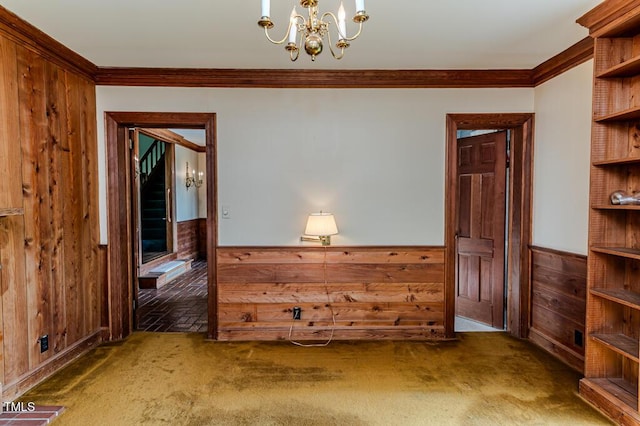 empty room featuring crown molding, wood walls, wainscoting, and a notable chandelier