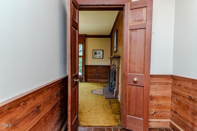 corridor featuring wooden walls, ornamental molding, and a wainscoted wall