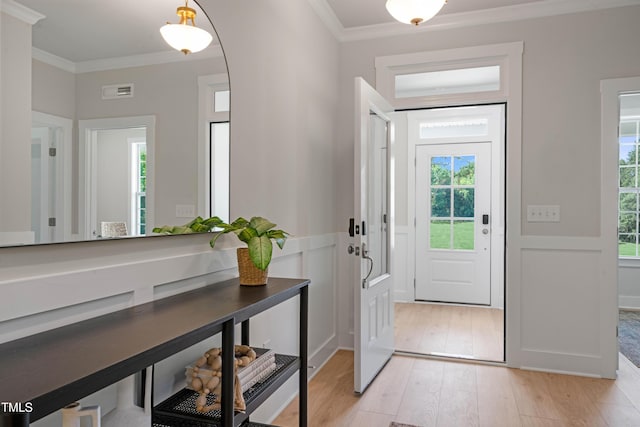 entryway with ornamental molding, a wealth of natural light, light wood finished floors, and a wainscoted wall