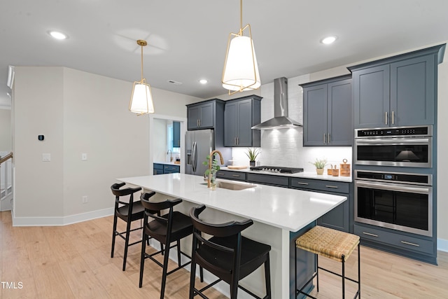 kitchen featuring a kitchen bar, appliances with stainless steel finishes, a sink, light countertops, and wall chimney exhaust hood