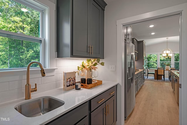kitchen with light stone countertops, stainless steel refrigerator with ice dispenser, tasteful backsplash, a sink, and light wood-style flooring