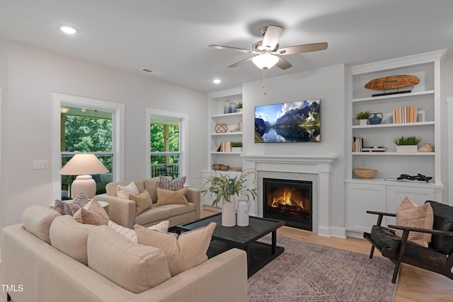 living area with a ceiling fan, visible vents, a high end fireplace, built in features, and light wood-style floors