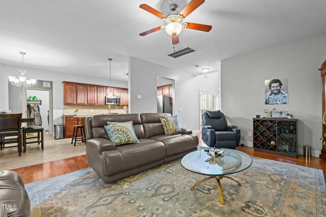 living room featuring a ceiling fan, a chandelier, and light wood-type flooring